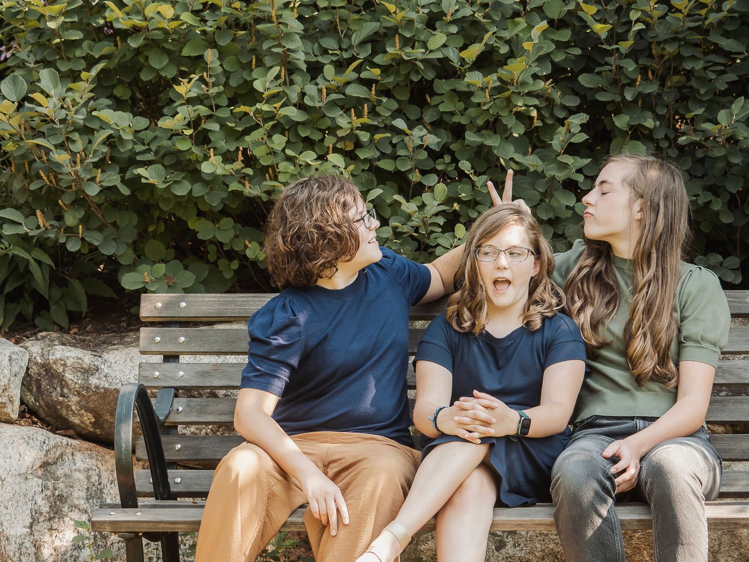 People sitting and laughing together on a wooden bench in garden setting while enjoying a casual outdoor moment.