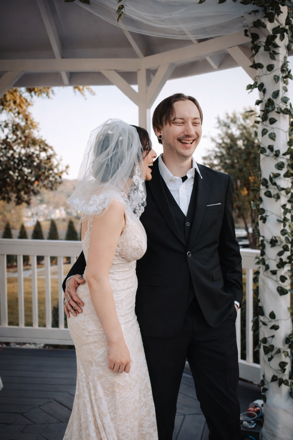 A joyful first look moment between a bride and groom at a white gazebo decorated with greenery.