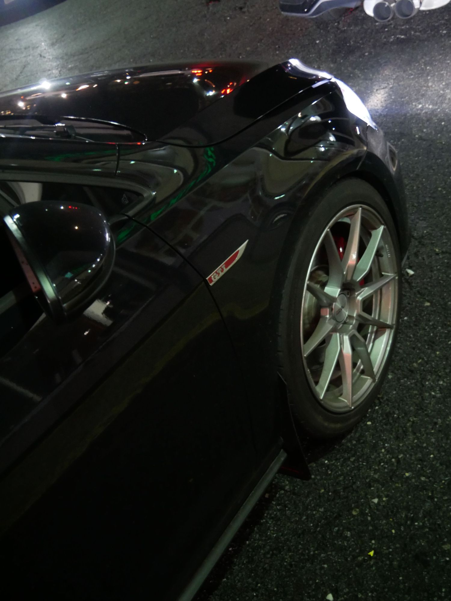 Black sports car fender detail at night showing alloy wheel and performance tire.