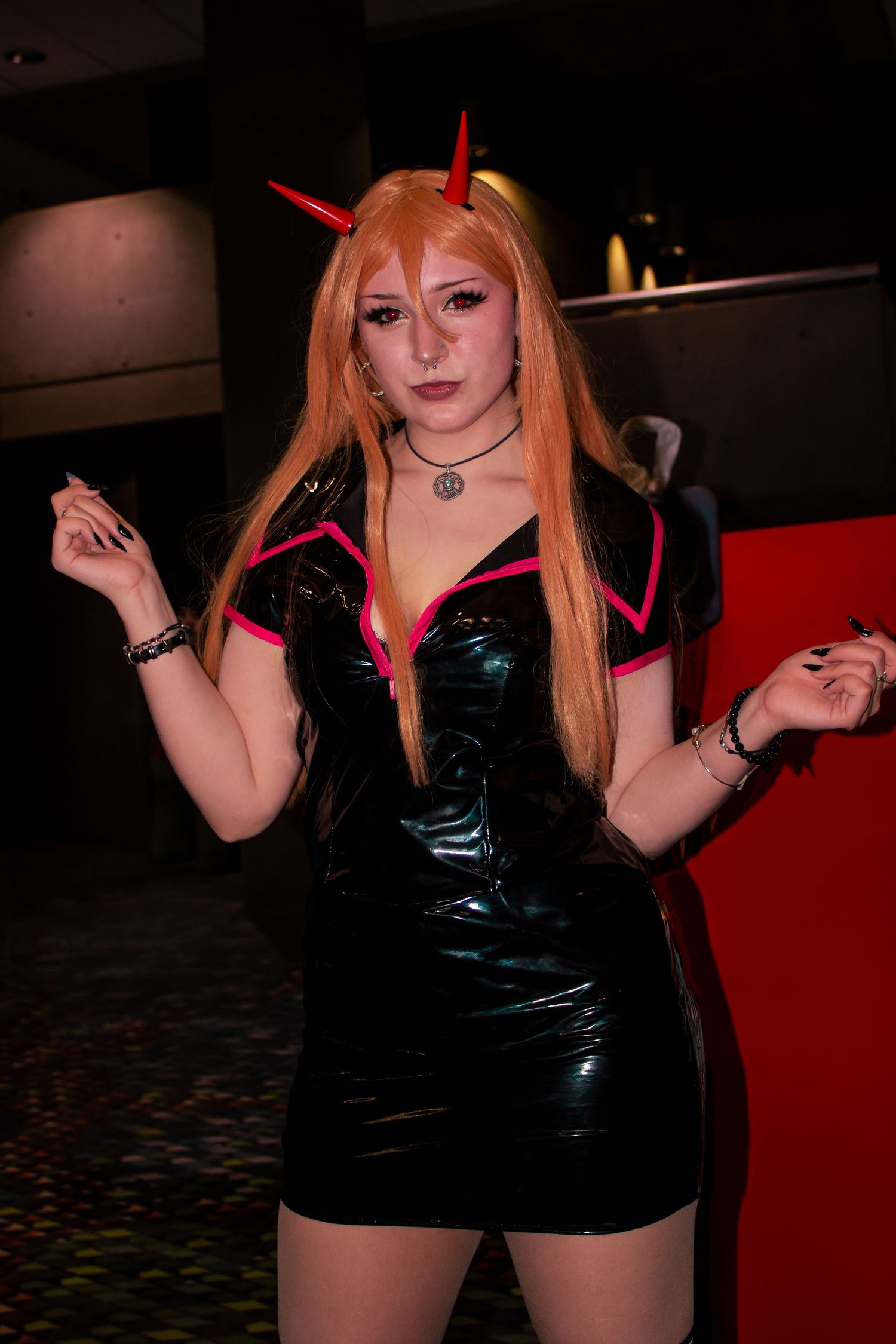 Cosplayer wearing black vinyl dress and long orange wig at convention.