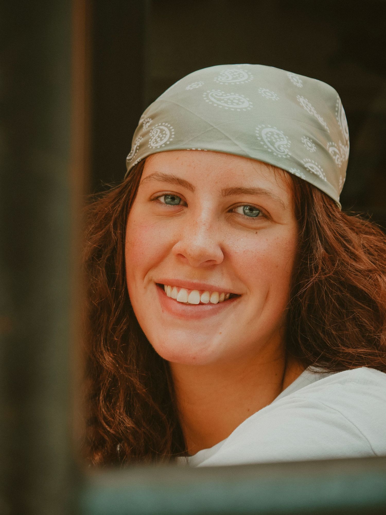Portrait of someone wearing a light green bandana and white shirt smiling warmly at the camera.