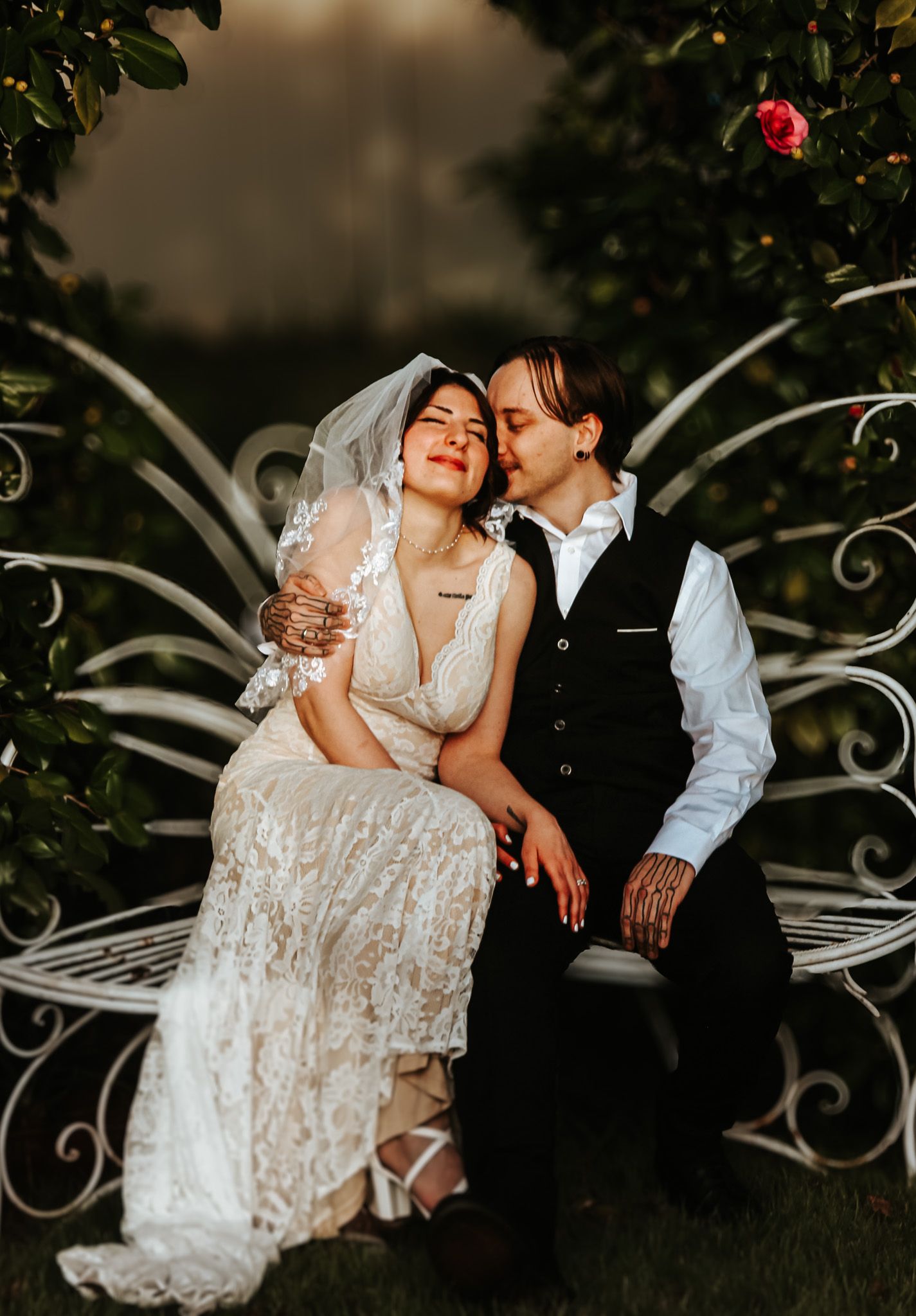 Romantic wedding couple embracing on ornate white garden bench.