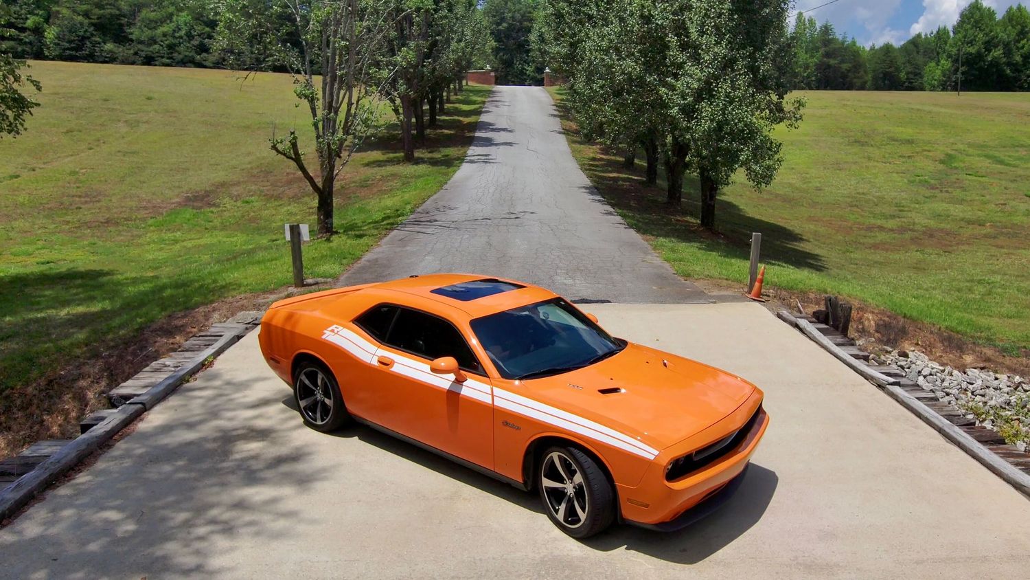 Orange performance vehicle photographed from multiple angles on a scenic driveway surrounded by greenery.