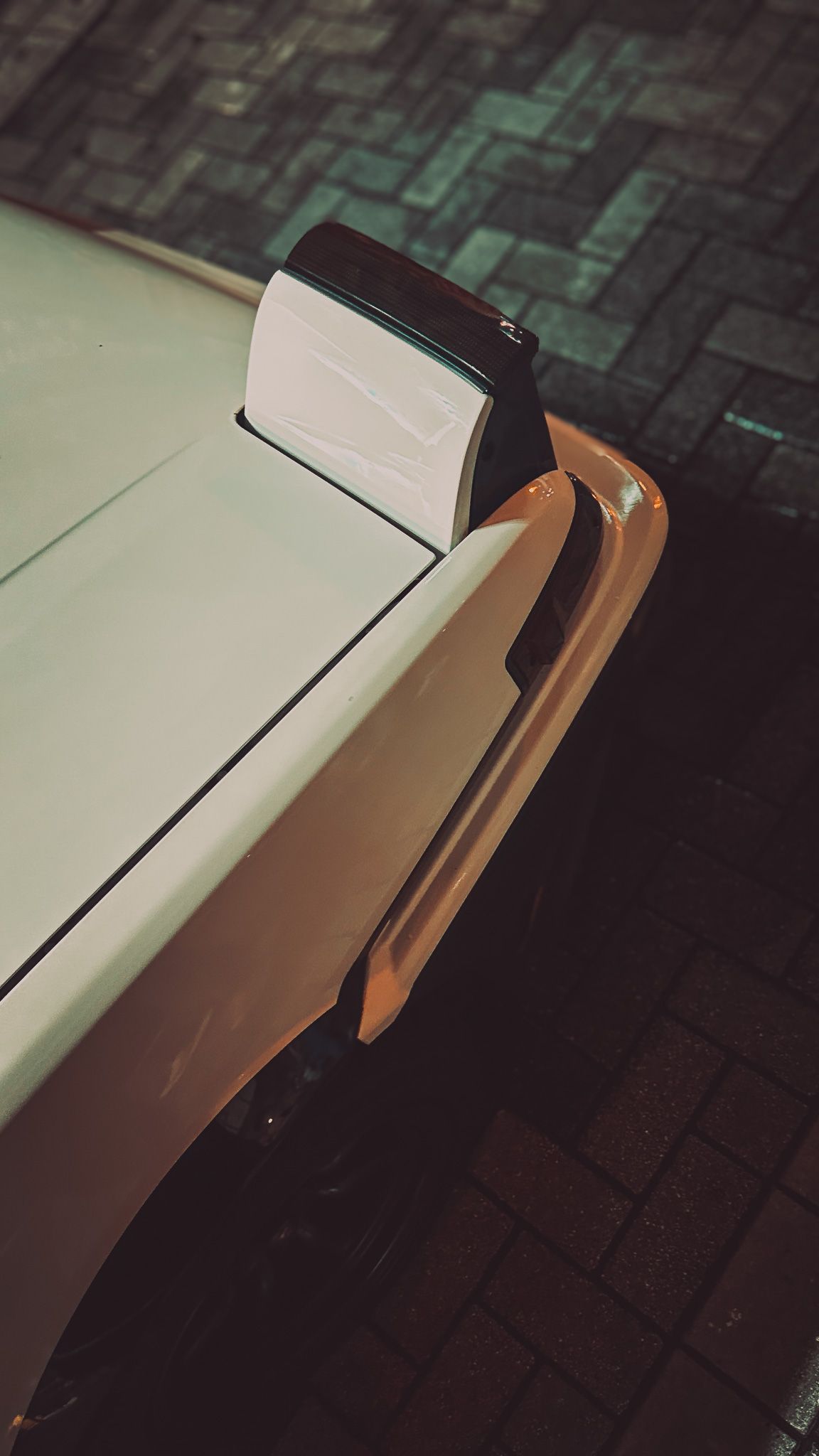 Close-up detail shot of white car hood and fender in low light.