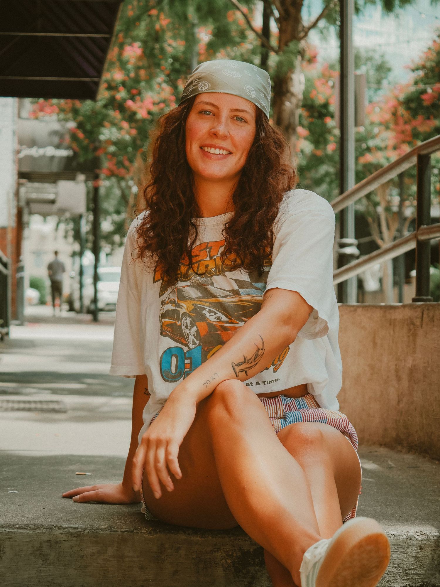 A casual skateboarding photoshoot featuring someone in a beanie cap and white t-shirt sitting outdoors on a sunny day.