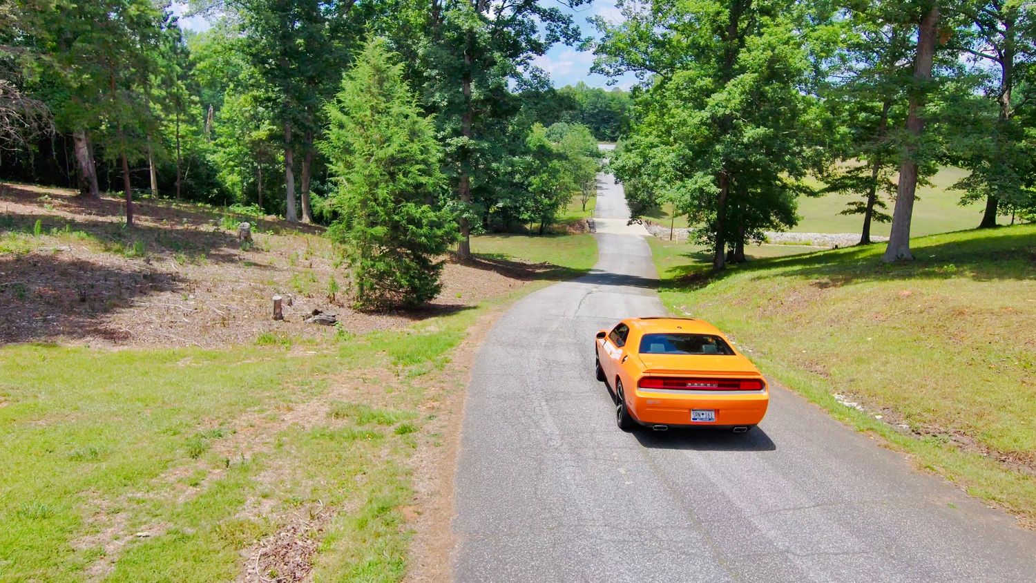 Panoramic sequence showing an orange sports car on a tree-lined driveway during daytime.
