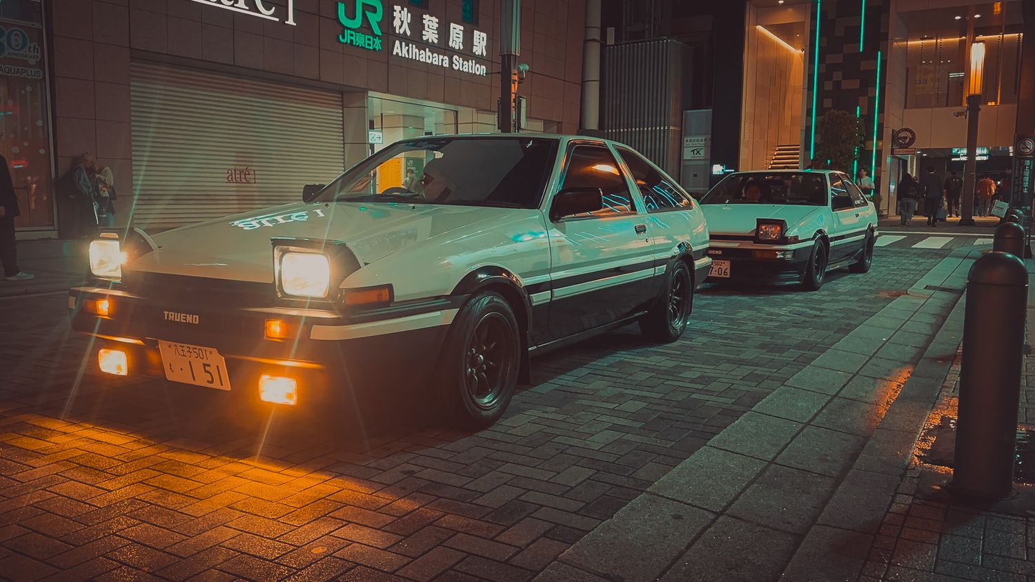 White sports car parked on brick pavement at night with urban signage in background.