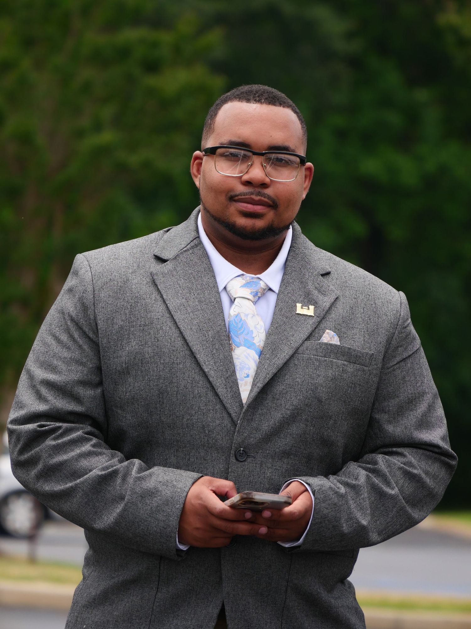 Professional in grey suit and light blue tie checks phone outdoors.