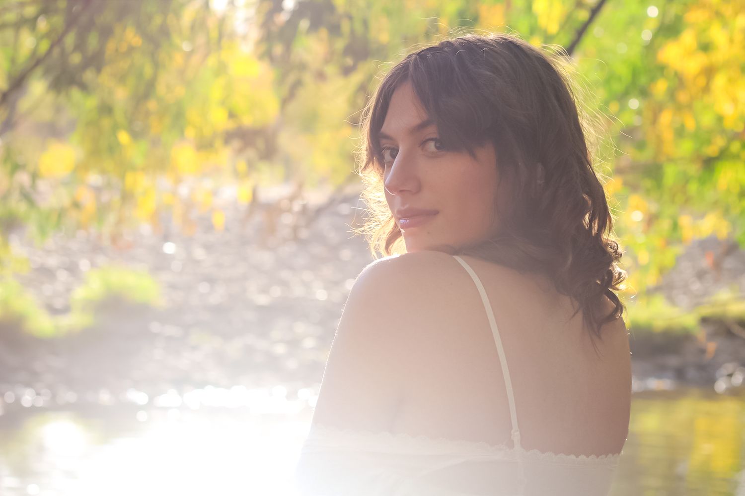 Ethereal outdoor portrait featuring soft sunlight and autumn foliage reflected in peaceful waters.