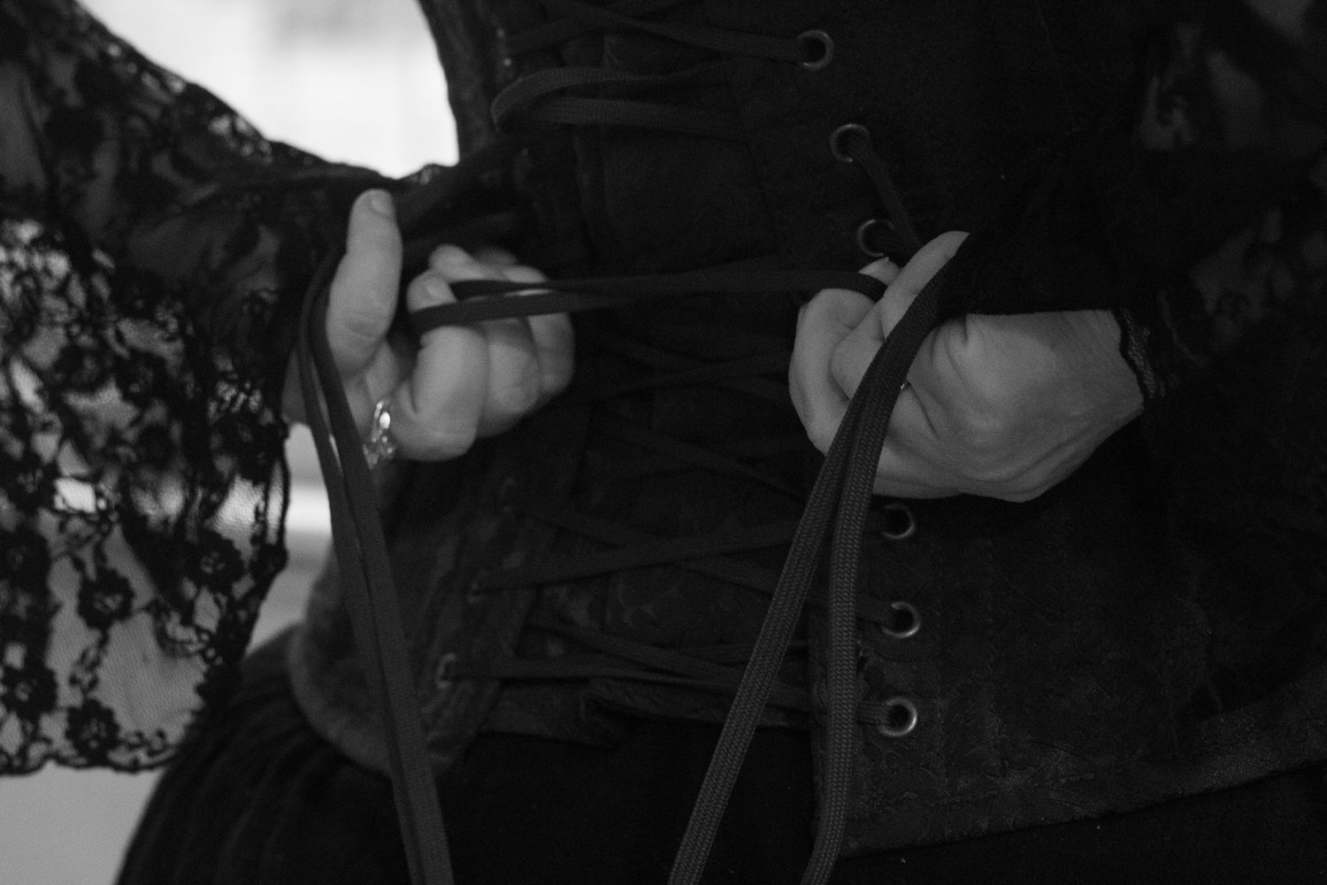 Close up black and white photo of a lace and corset bodice with delicate details and ribbons