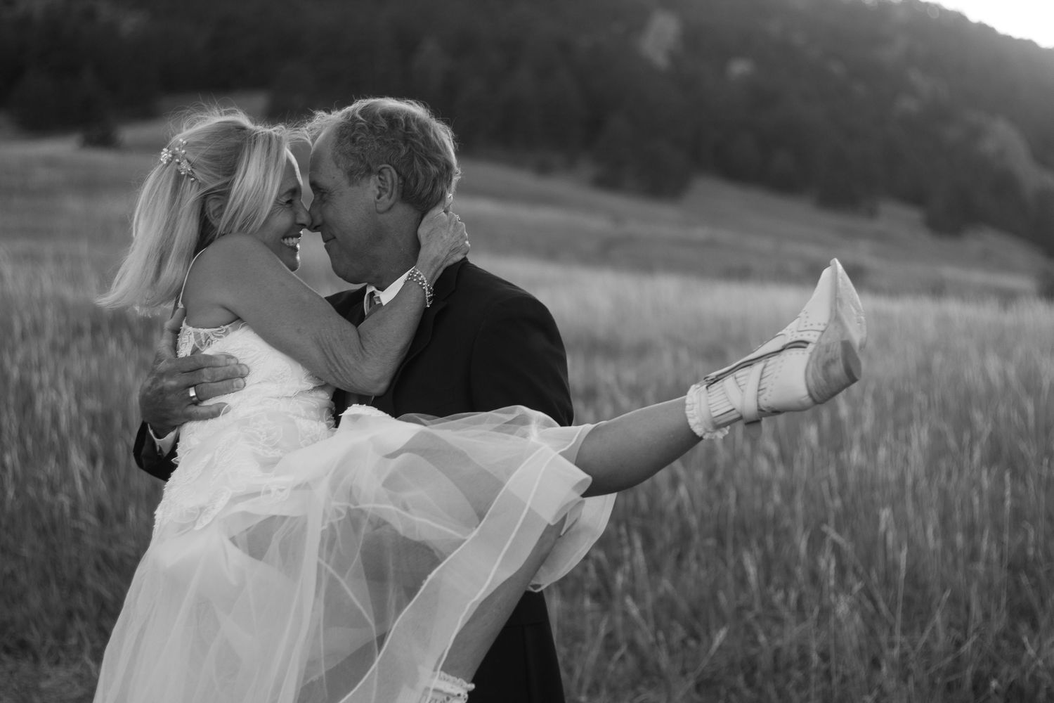 A groom carries his new wife in Boulder, Colorado amongst the fields and mountains of the flatirons
