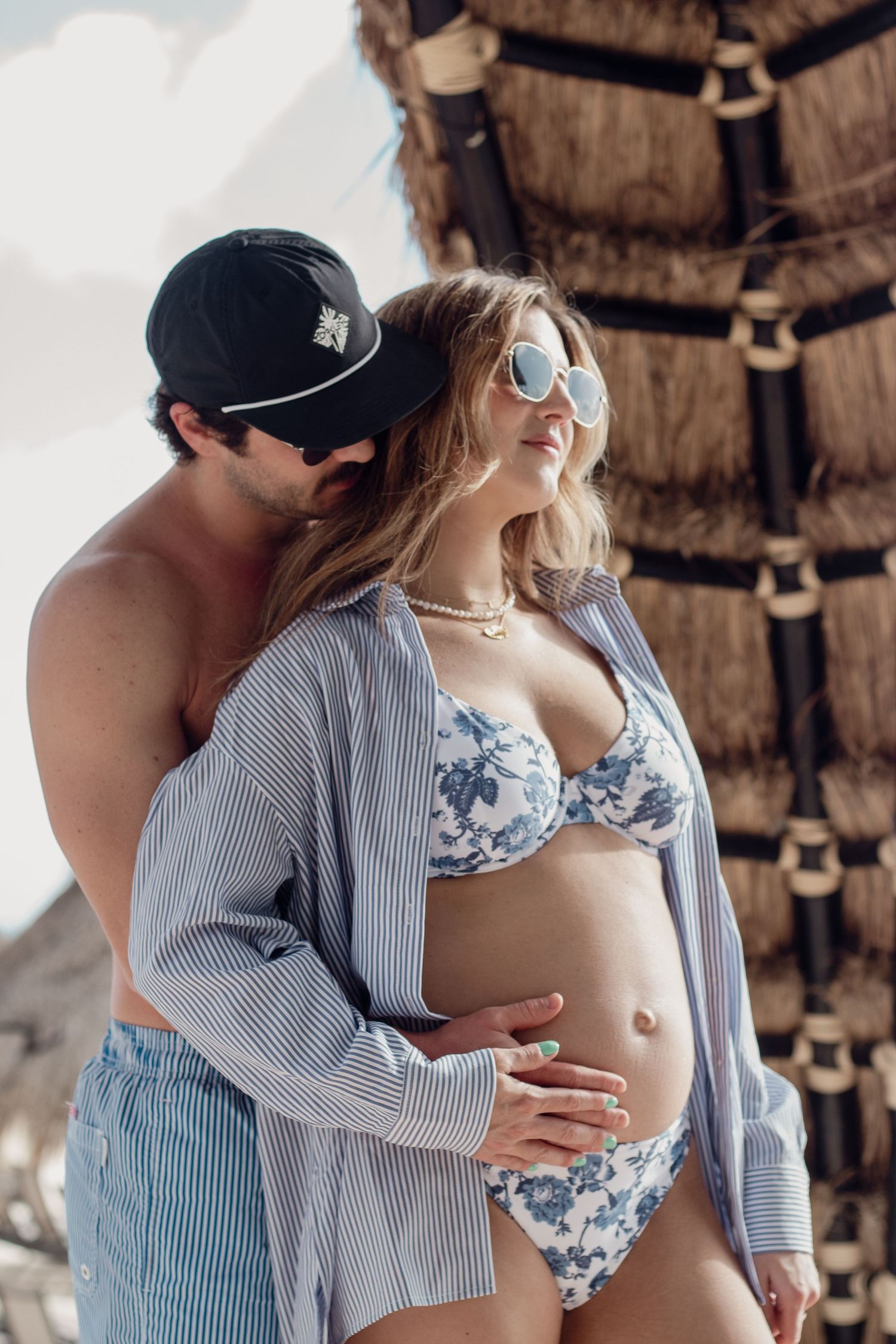 A couple shares an intimate embrace on a beachfront deck with rustic wooden beams and natural lighting.