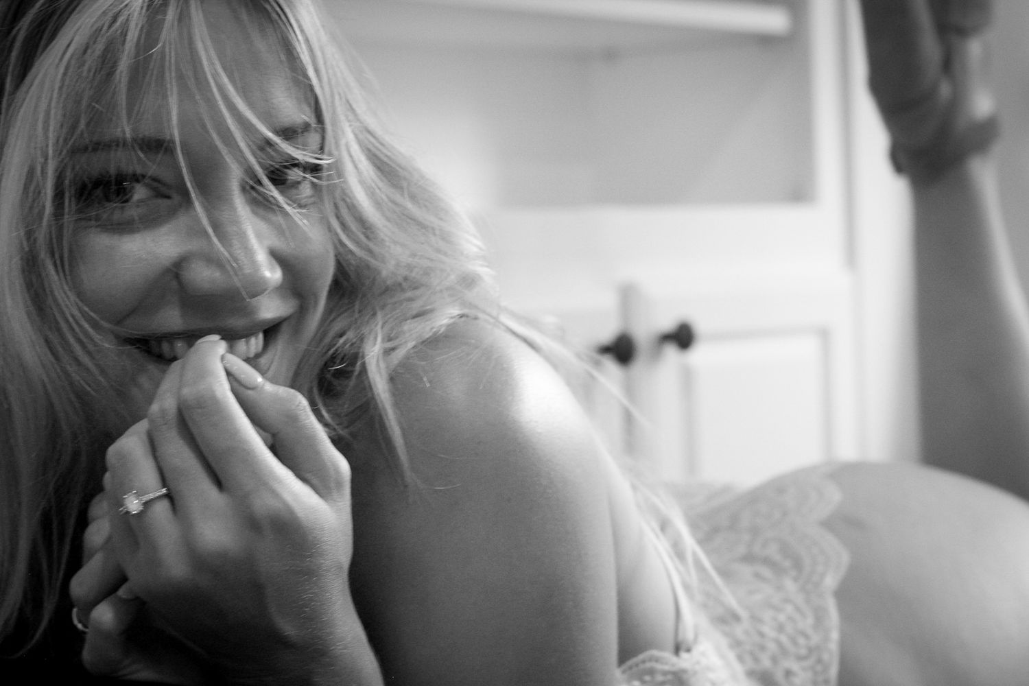 Intimate black and white portrait capturing someone with light hair and a natural smile in soft bedroom lighting.