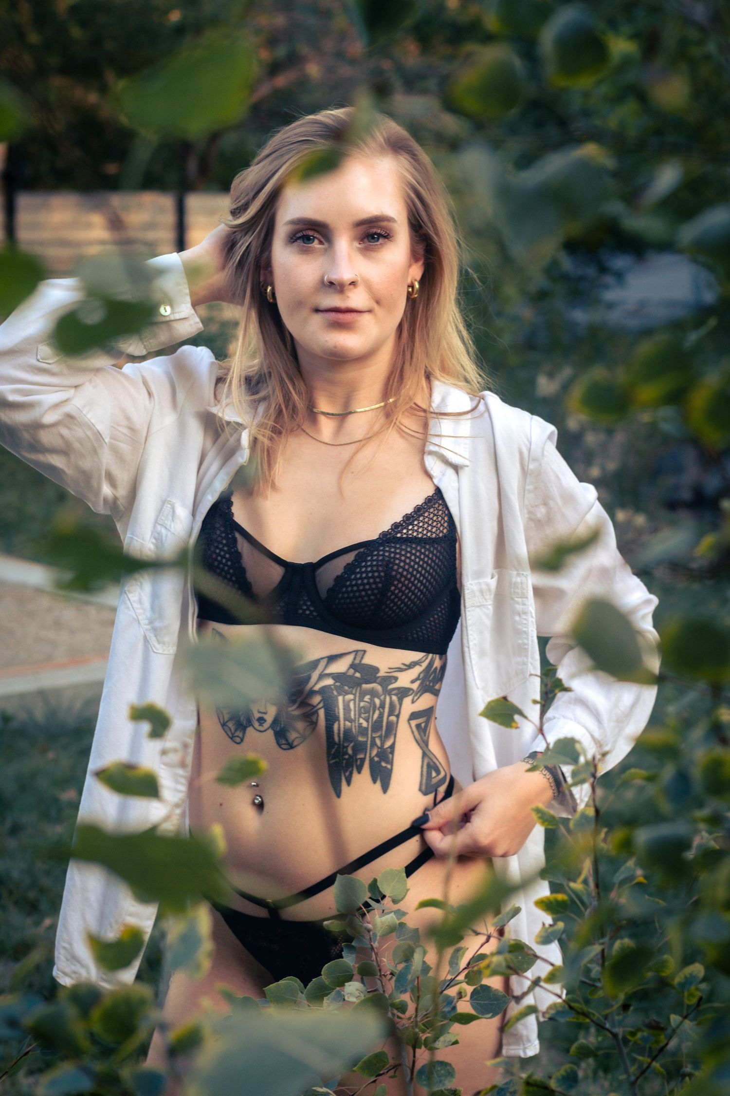 Fashion portrait showing white cropped jacket and black mesh top against natural outdoor foliage backdrop.