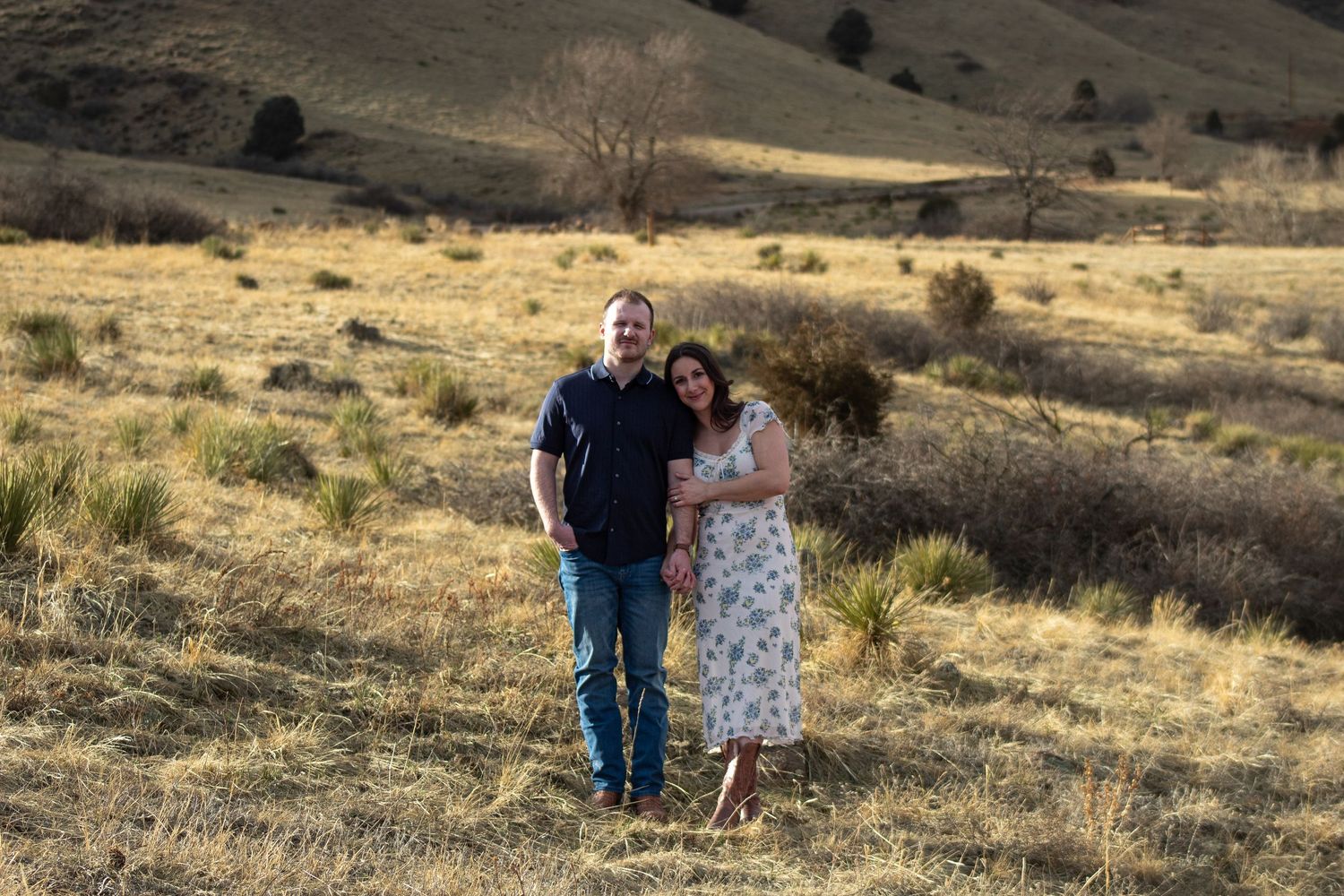 Two people walk together across a golden grass hillside at Red Rocks during a sunset photo session.
