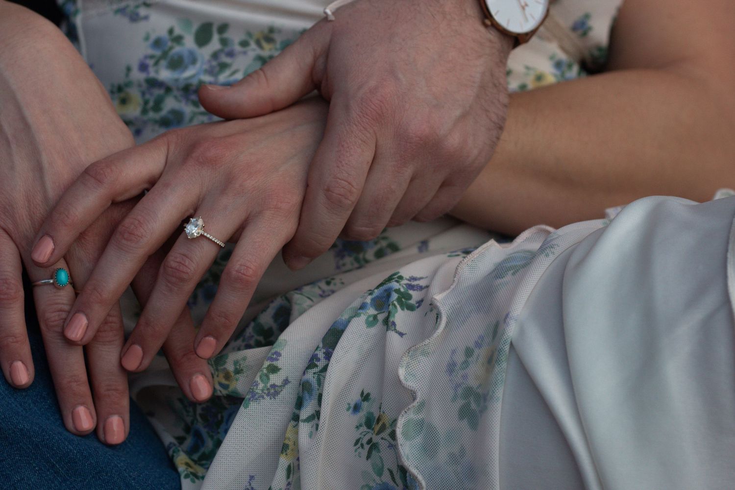 Close-up photo of hands showing engagement ring details in a romantic wedding dress setting.