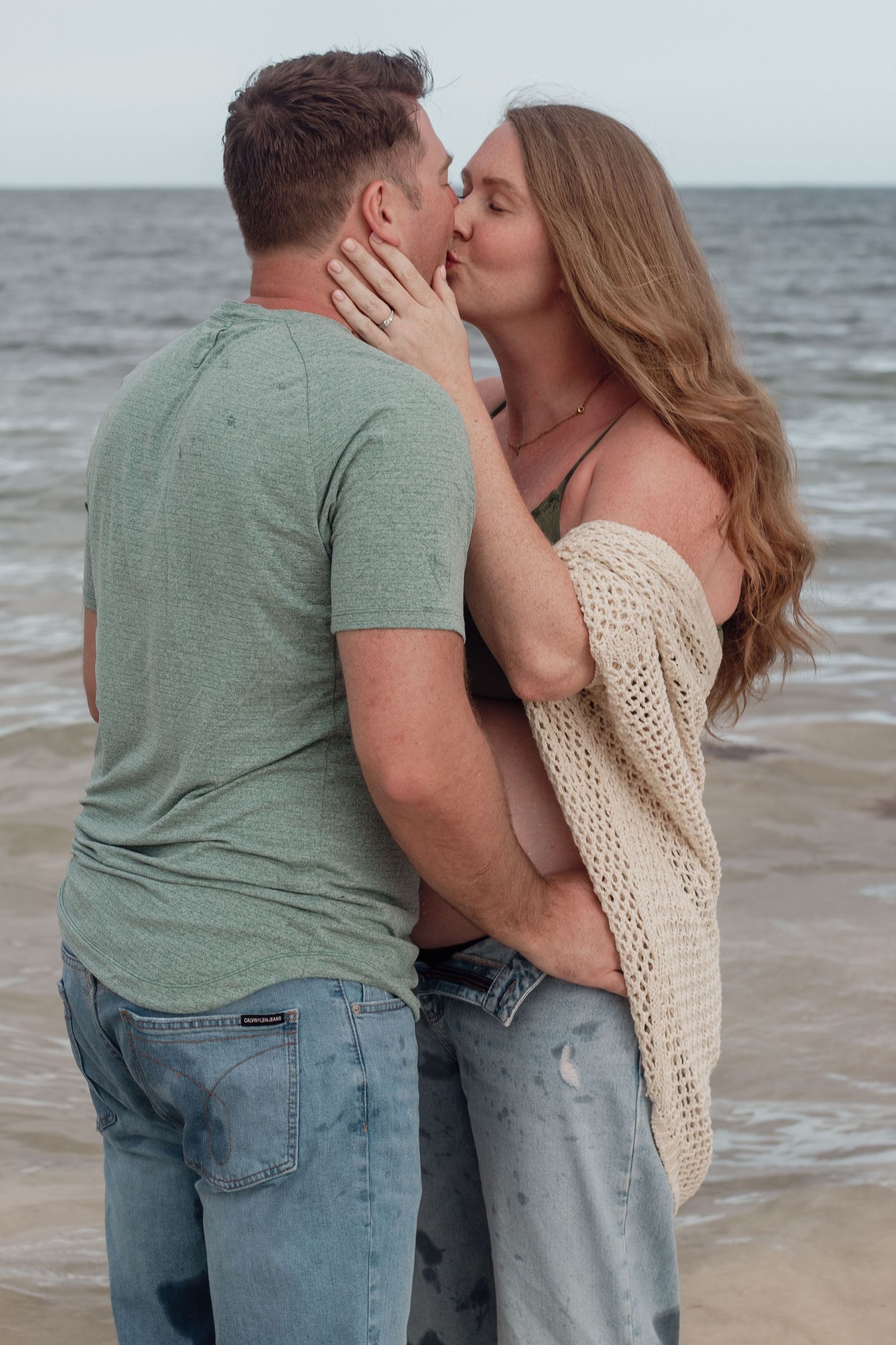 A romantic couple sharing intimate moments and kisses while standing together on a beach near the ocean.