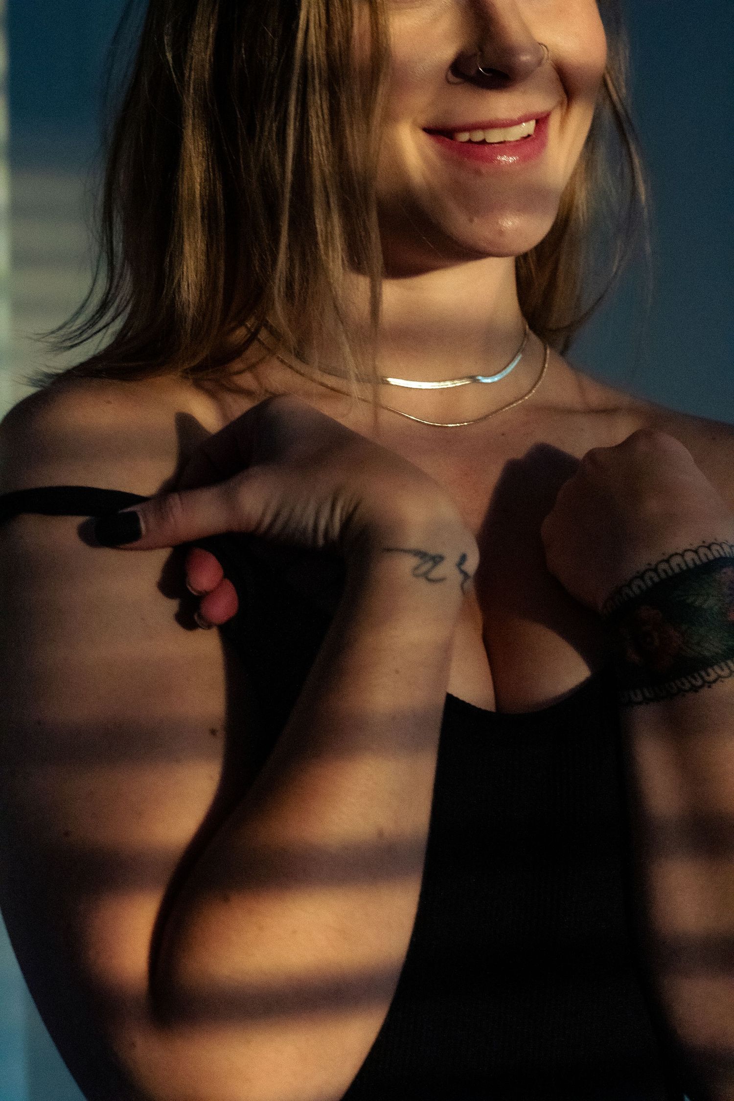 Cropped artistic portrait showing shadows and a delicate gold necklace against bare shoulders in moody lighting.