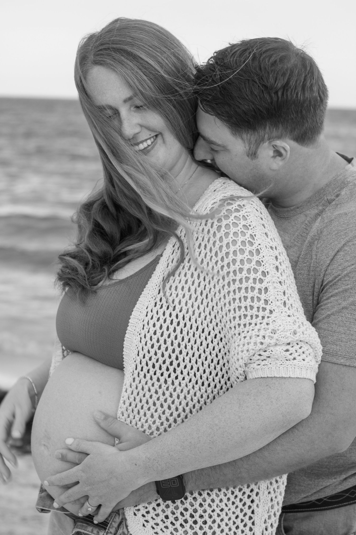 Black and white photo of a romantic beach embrace with a woman in crochet top and her partner at sunset.