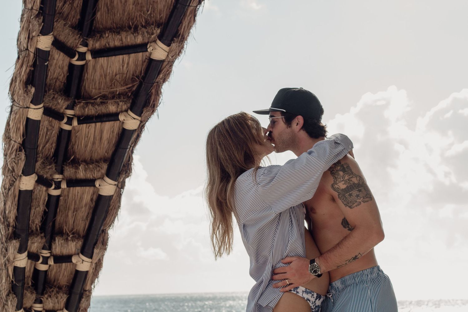 A couple embraces in romantic silhouettes against a beachy backdrop at sunset.