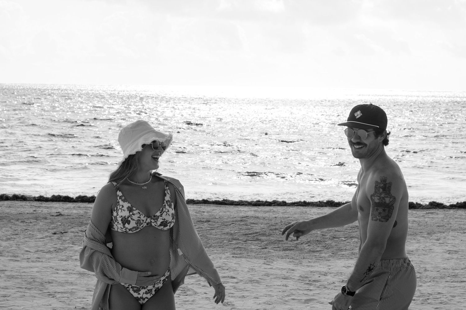 A black and white beach scene shows two people walking along the shoreline with the ocean visible in the background.