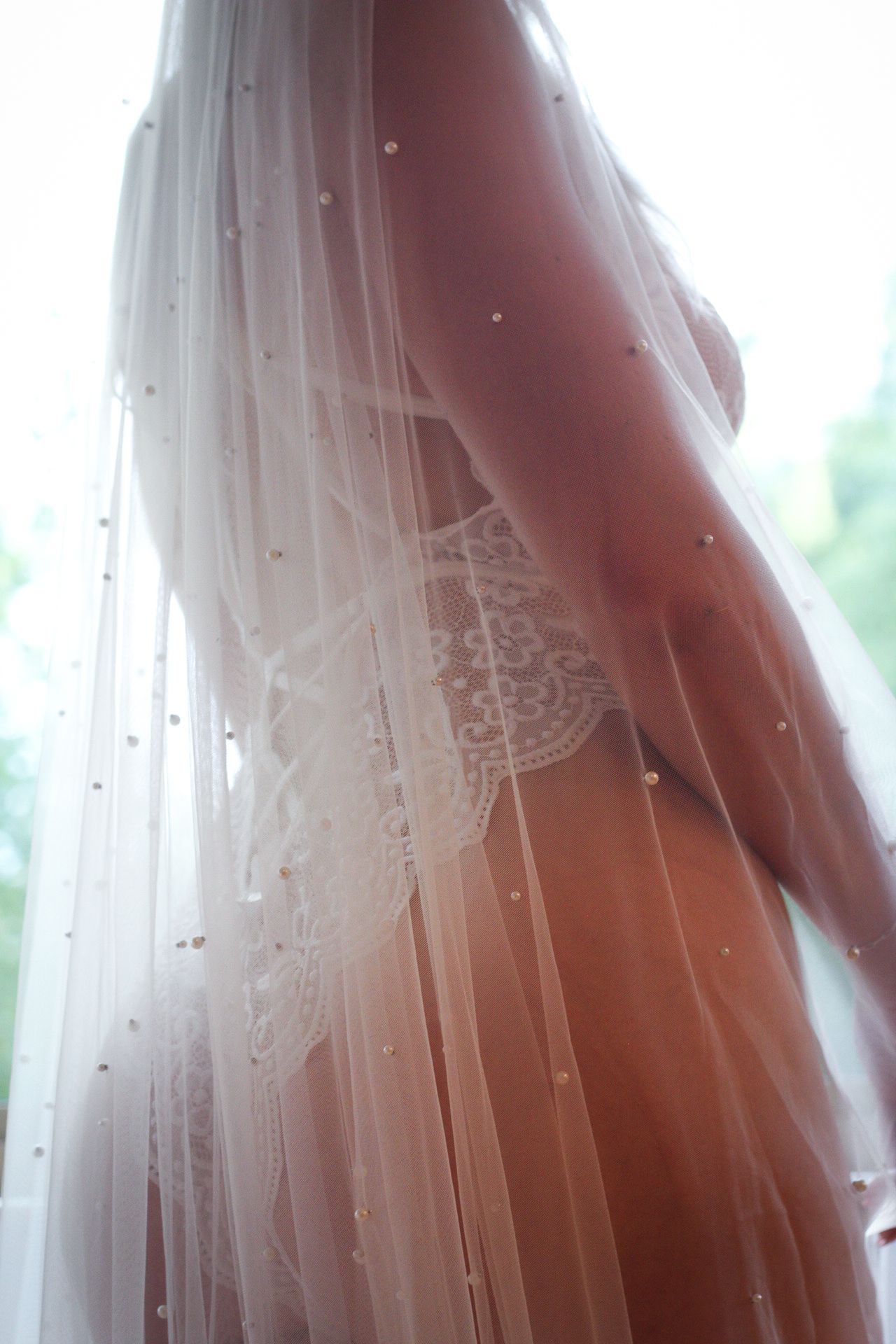 Delicate white wedding veil drapes across a woman's backside while wearing a white lace lingerie set