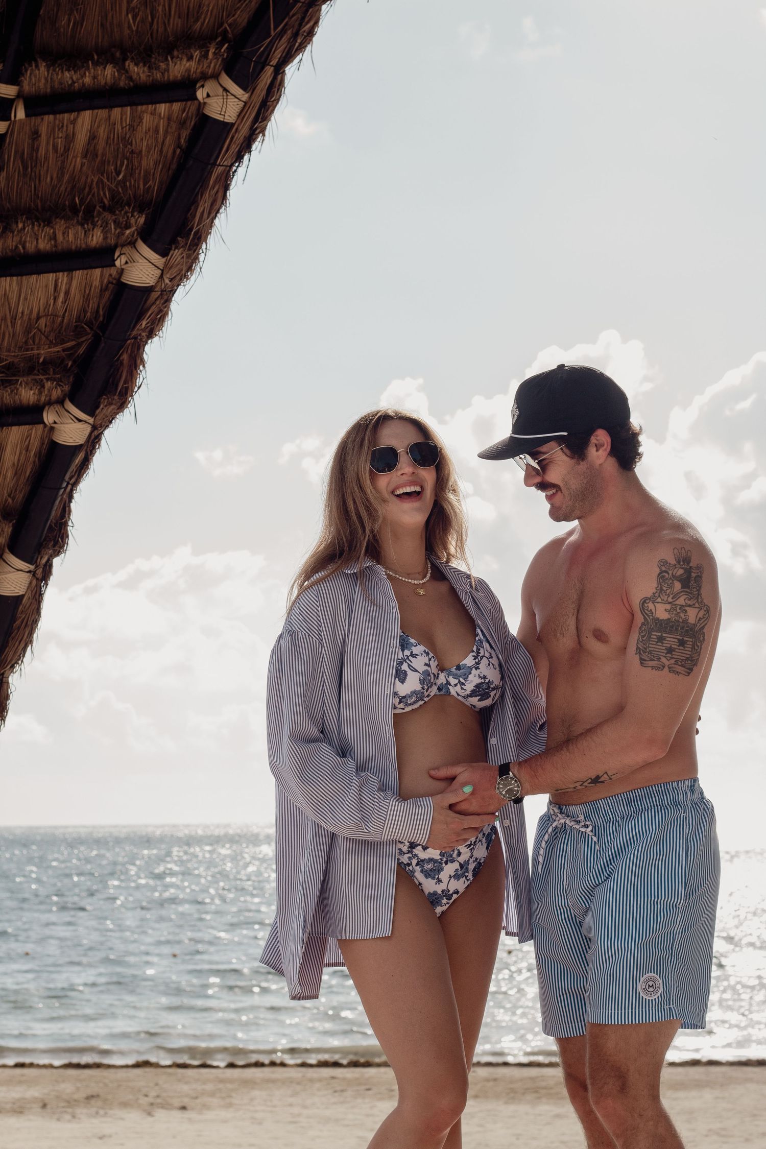 Two people enjoying a romantic moment together under a thatched beach umbrella by the ocean.