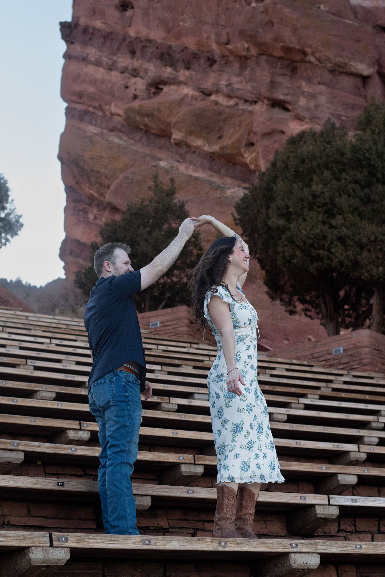 A couple dances together on wooden benches at Red Rocks Amphitheatre in Colorado against a scenic backdrop.
