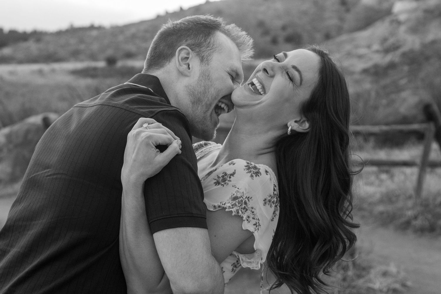 A candid black and white photo captures a joyful couple sharing an intimate laughing moment together outdoors in Red Rocks Ampitheatre