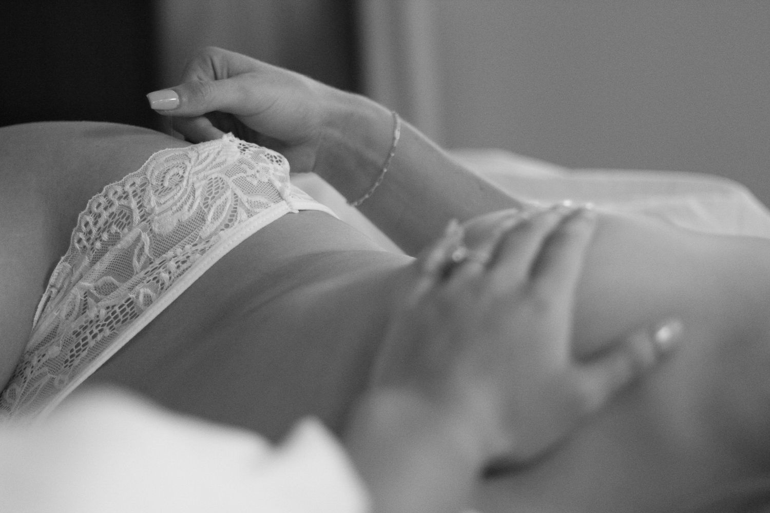 A black and white close-up photograph showing hands resting on lace lingerie.