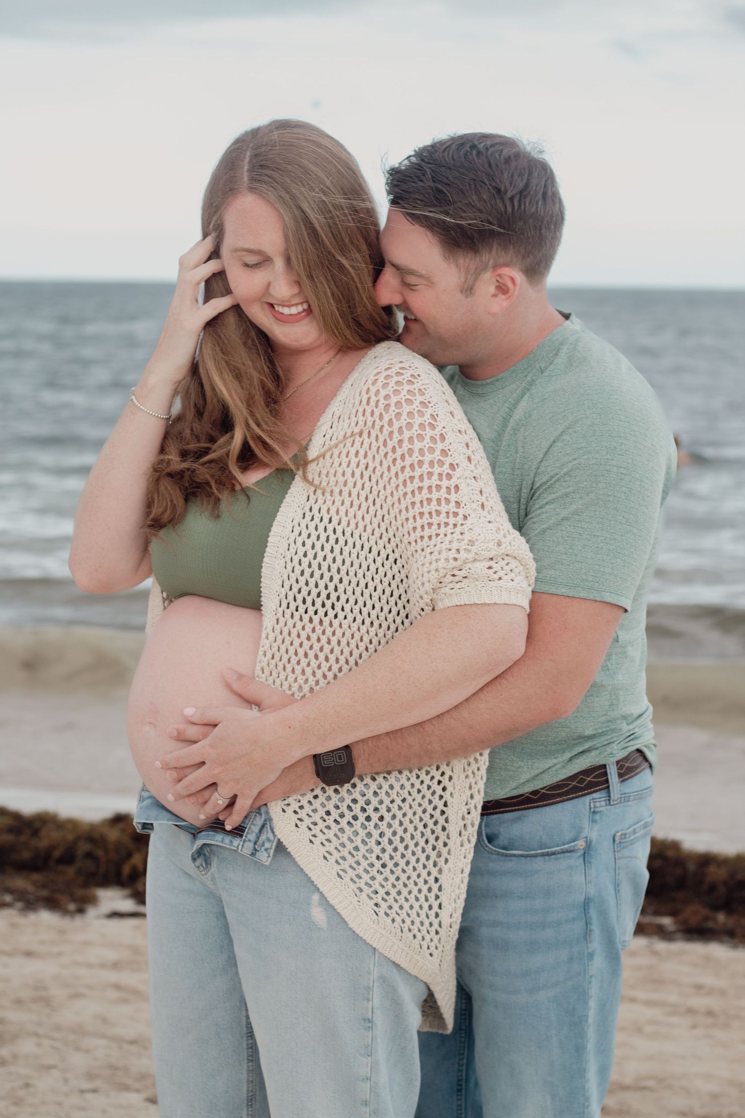 A couple shares intimate moments on the beach at sunset while wearing casual coastal attire.