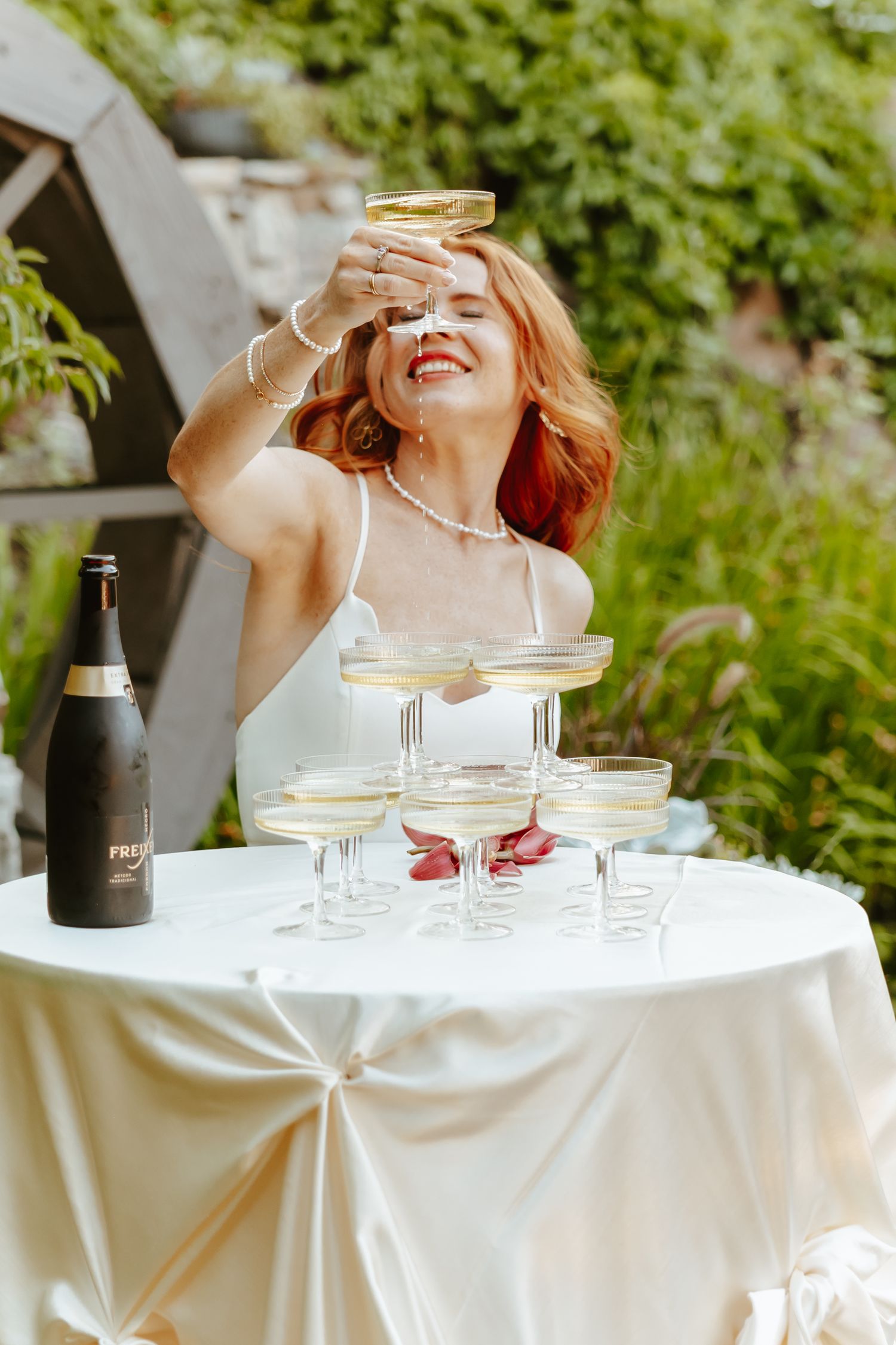 A joyful moment in white at a garden party with stacked champagne glasses and sparkling wine on an elegant table.