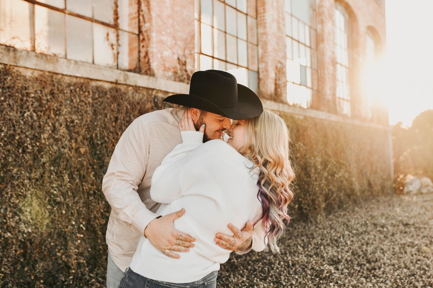 Editorial engagement portrait of a couple kissing at sunset at The Cotton Mill, blending warm light with modern industrial style