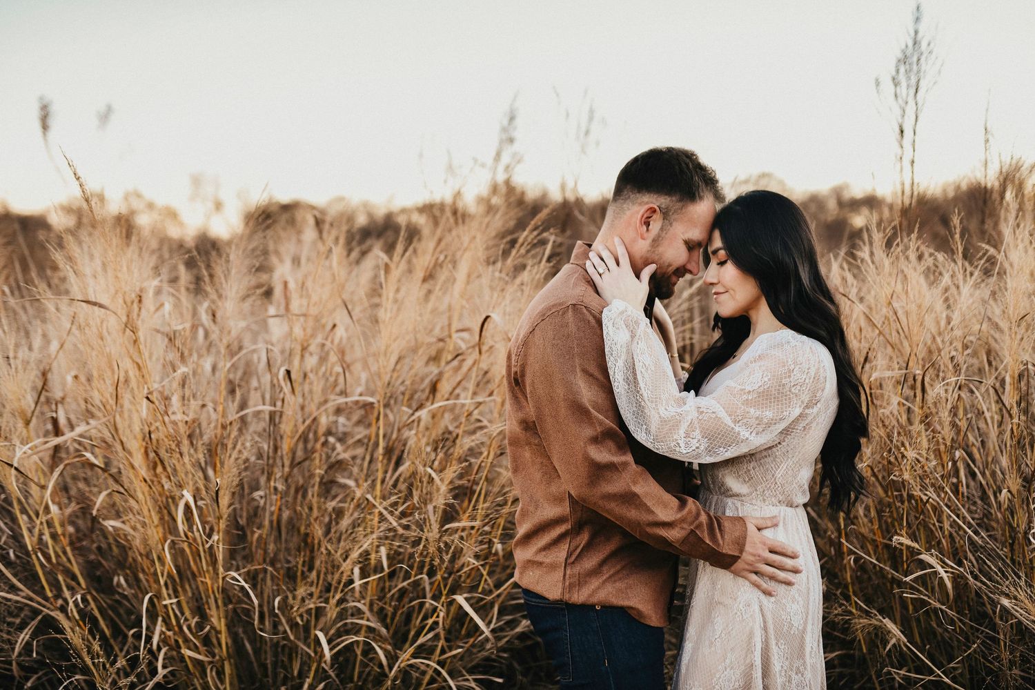 Couple sharing an intimate moment with heads together during an engagement session in a Little Elm field.