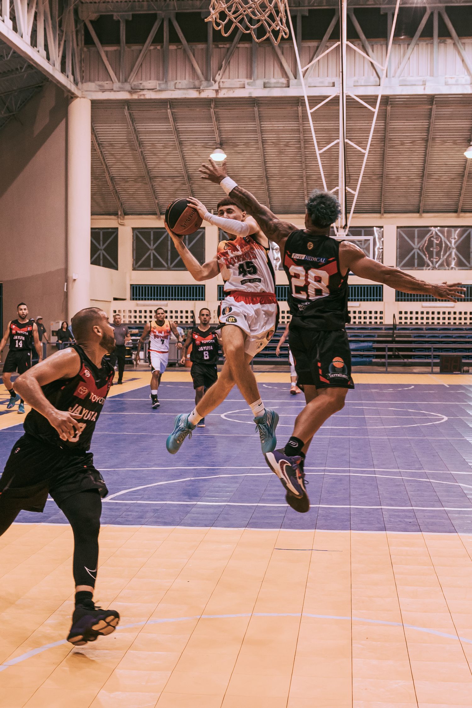 Basketball players compete in an indoor game, with player #28 defending against a layup attempt.