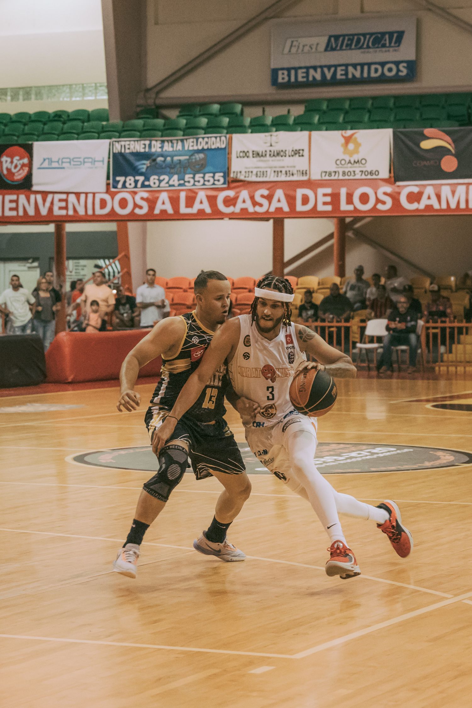 Two basketball players compete on a hardwood court in Puerto Rico, with one player in white dribbling past a defender in black.
