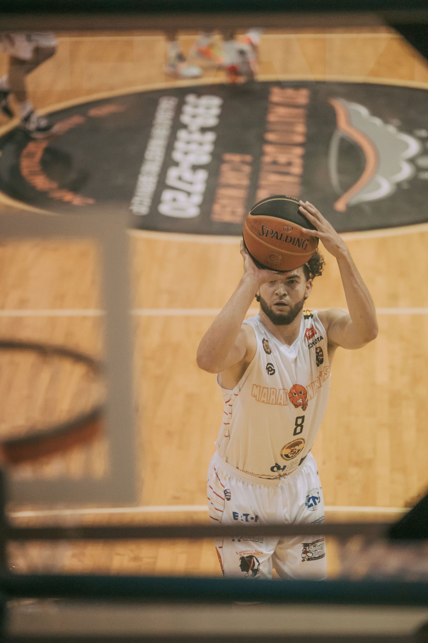 Basketball player in white jersey number 8 preparing to shoot, holding Spalding ball overhead on indoor court.