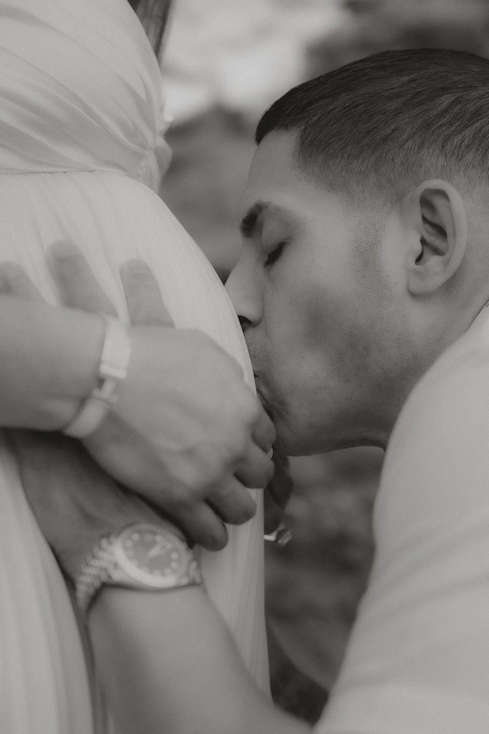 Black and white close-up of an expecting father kissing his partner's baby bump