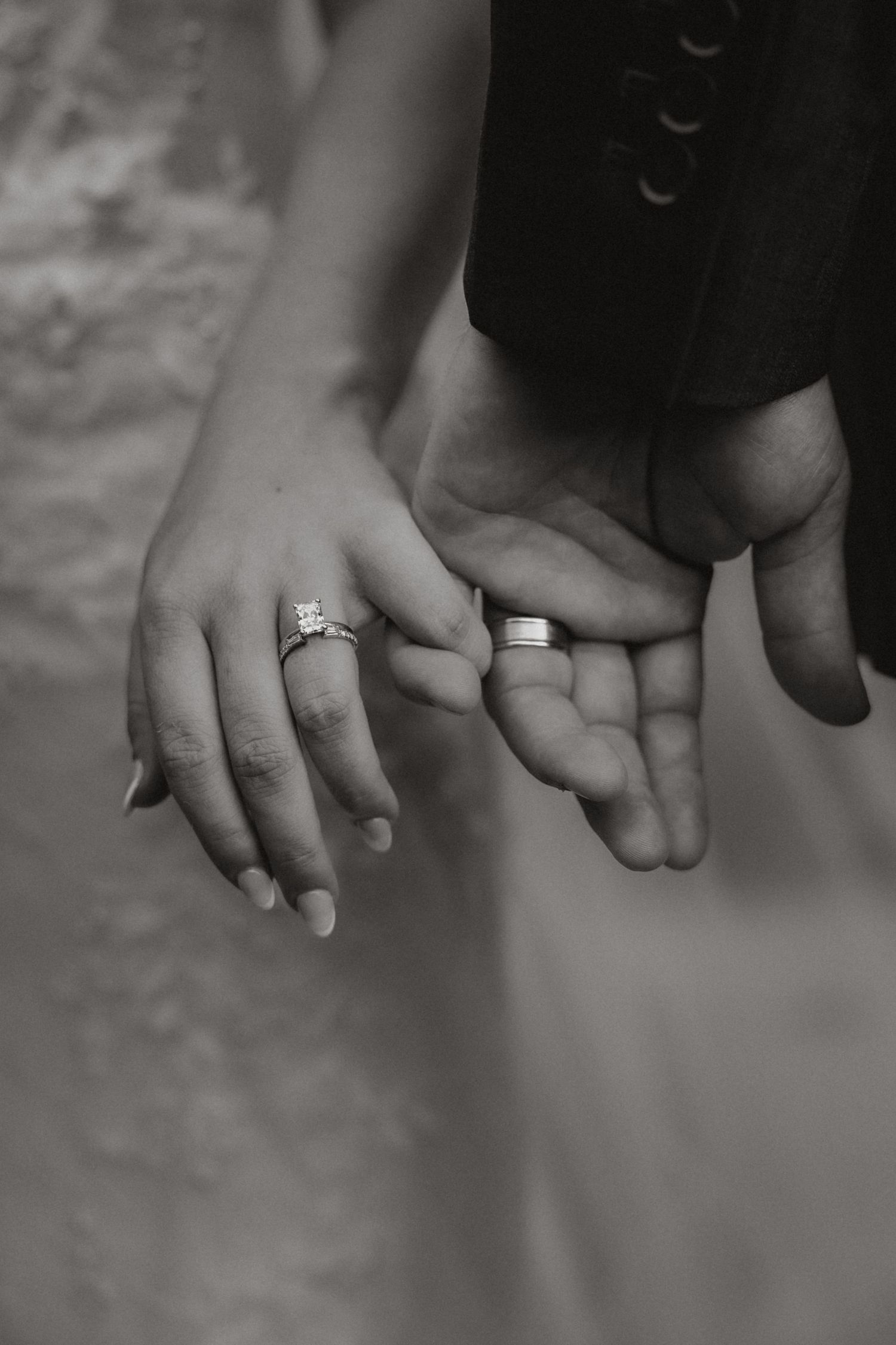 Black and white detail of newlyweds holding hands and showing their wedding rings
