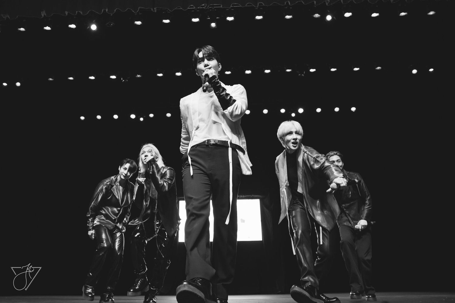Black and white photo of five performers on stage under spotlights during a live concert performance.