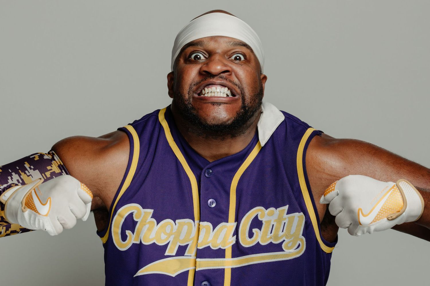 Man in Choppa City purple baseball jersey and white headband posing aggressively with fists forward.