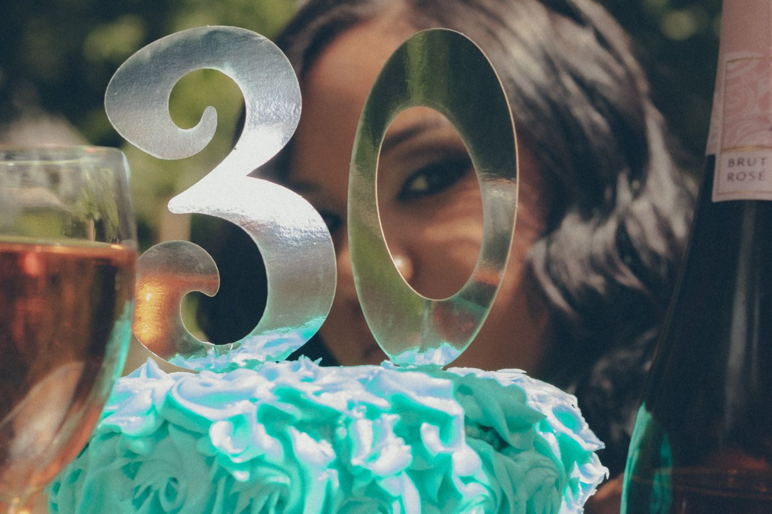 A woman celebrating her 30th birthday with a teal ruffled cake topped with a silver number 30 cake topper.