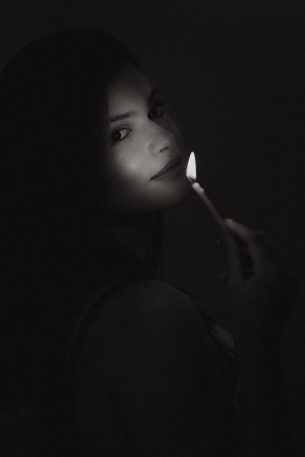 Black and white birthday portrait of a woman holding a lit candle beside her face in dramatic low-key lighting