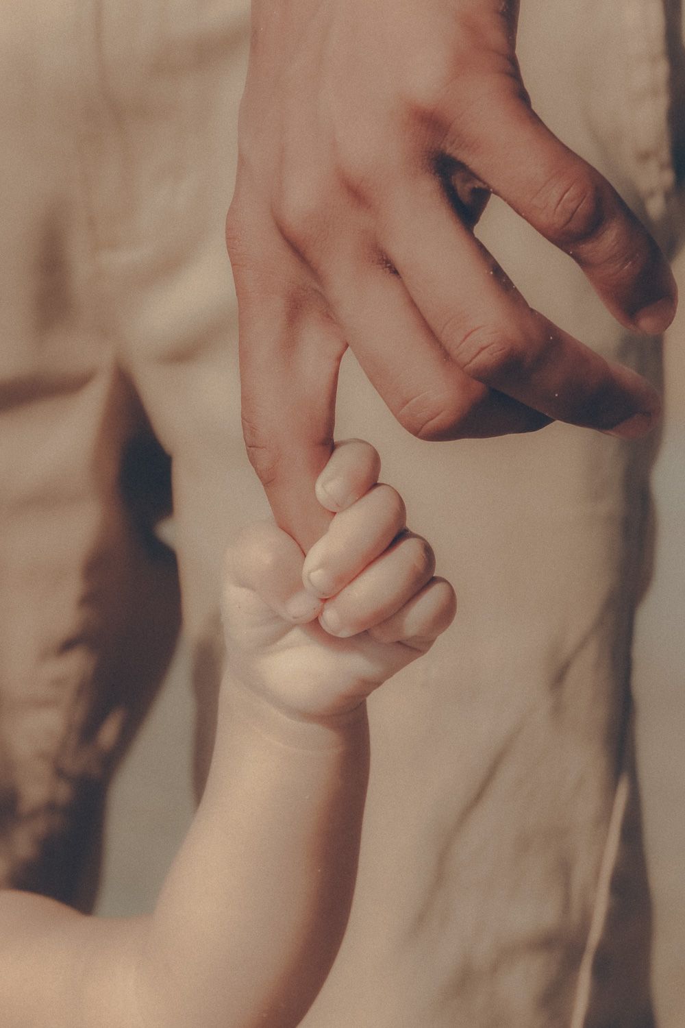 Close-up family photo of a baby's tiny hand wrapped around an adult's finger