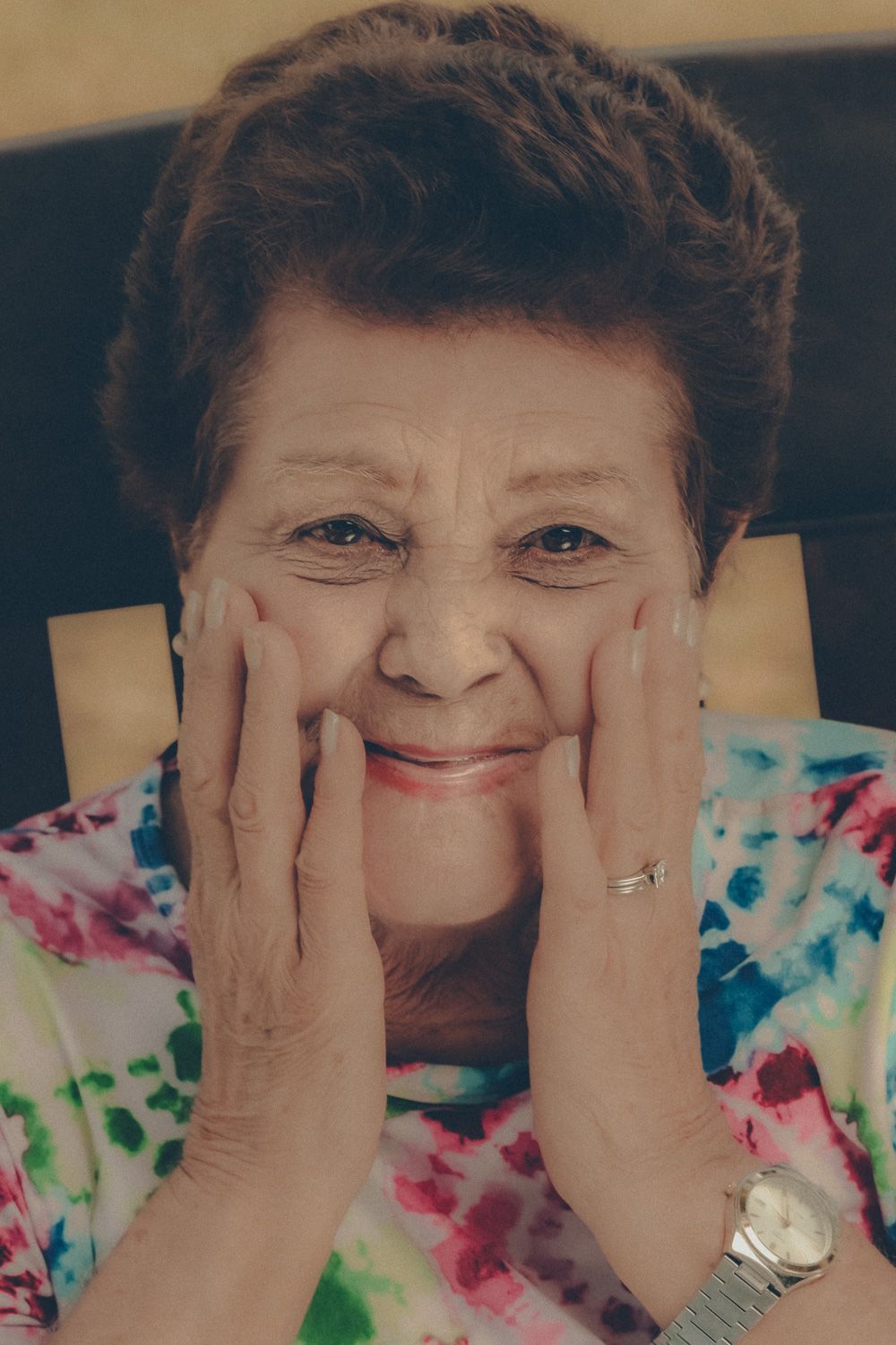 Joyful birthday portrait of an older woman smiling at the camera with her hands gently framing her face