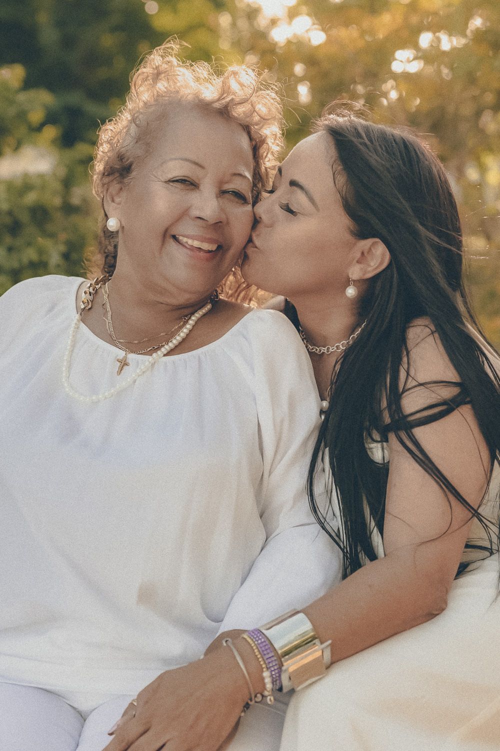 Candid multigenerational family portrait of a younger woman kissing an older woman on the cheek outdoors