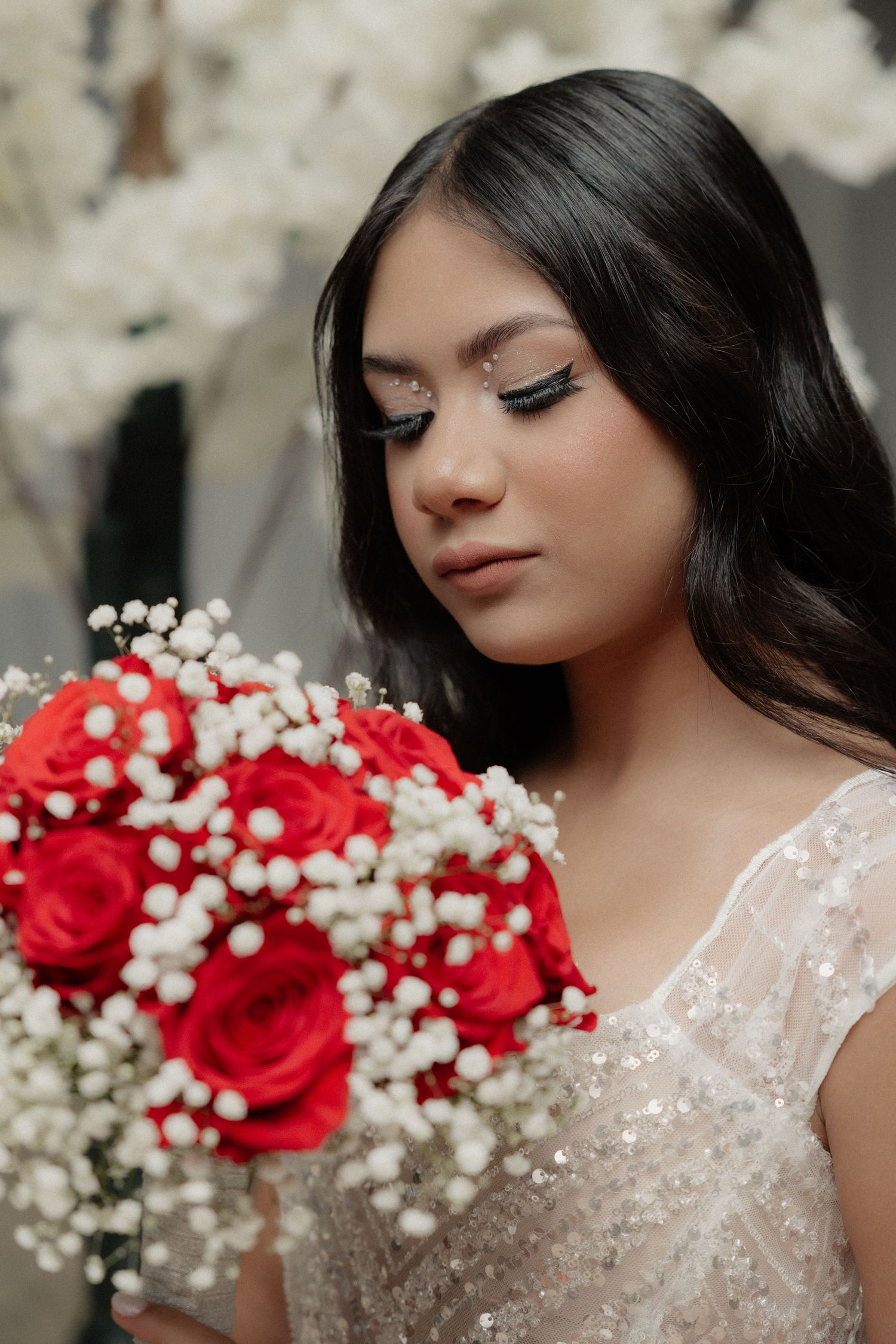 Close-up birthday portrait of a teenage woman with dramatic eye makeup posing behind a bouquet of red flowers