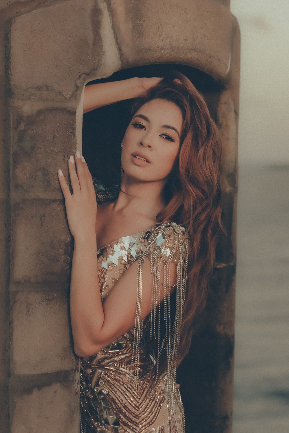 Glamour portrait of brunette model wearing an embellished gold dress beside a stone archway