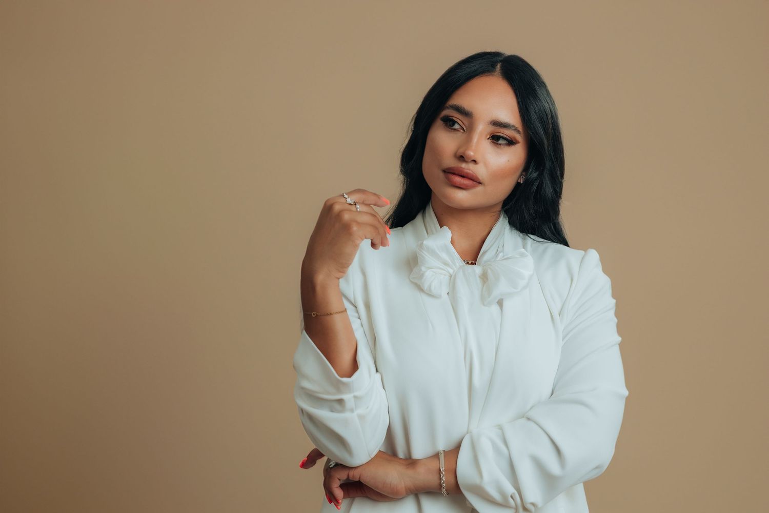 A young woman in a white ruffled blouse poses confidently against a warm beige background.