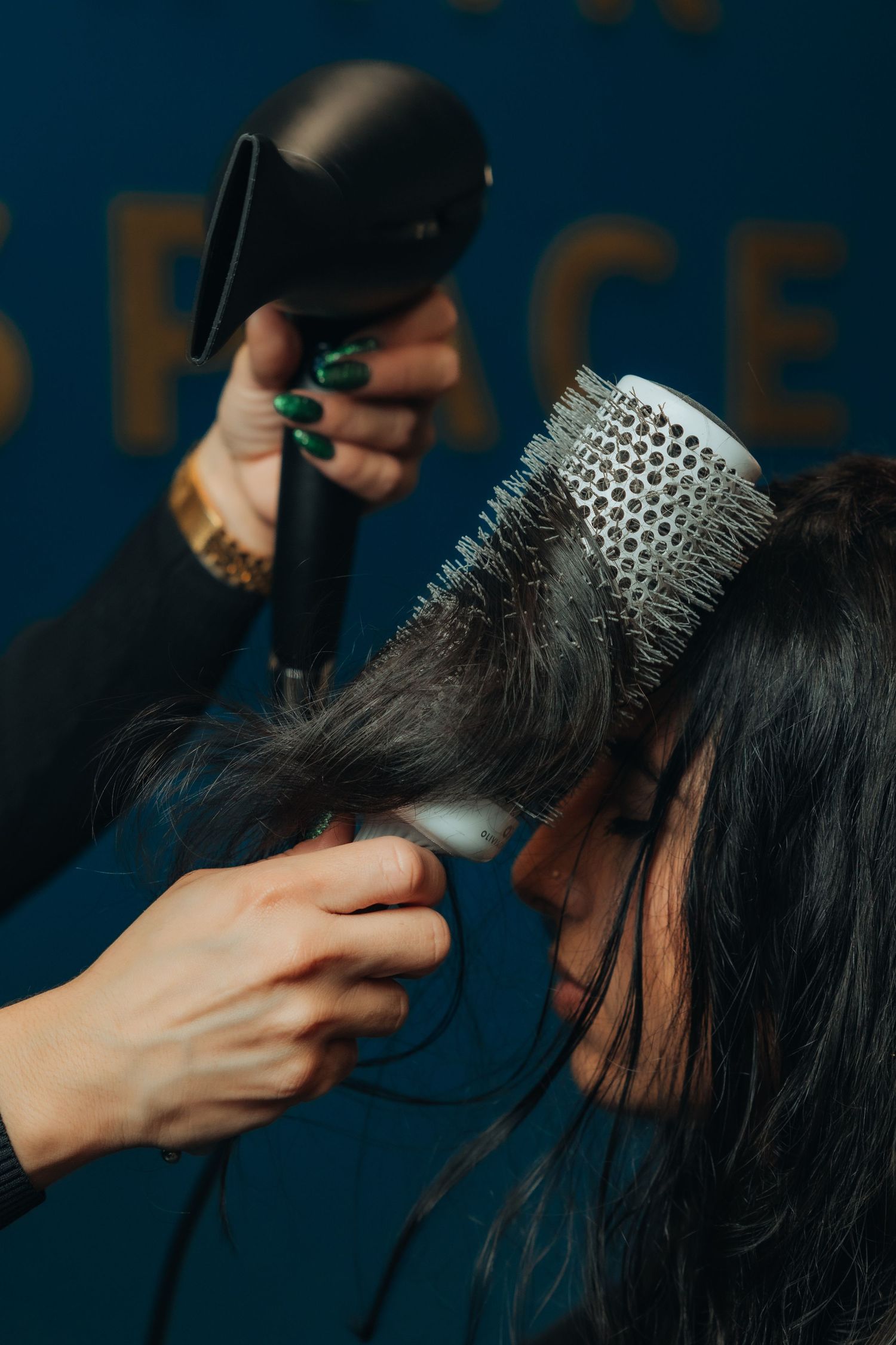Hairstylist blow drying dark hair with round brush at a professional salon.